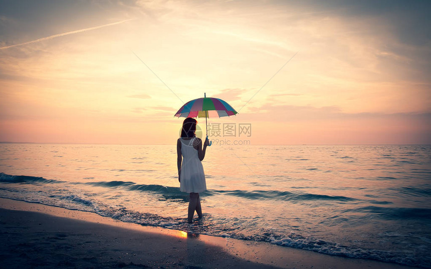日出时带着伞在海滩上的年轻漂亮女孩图片