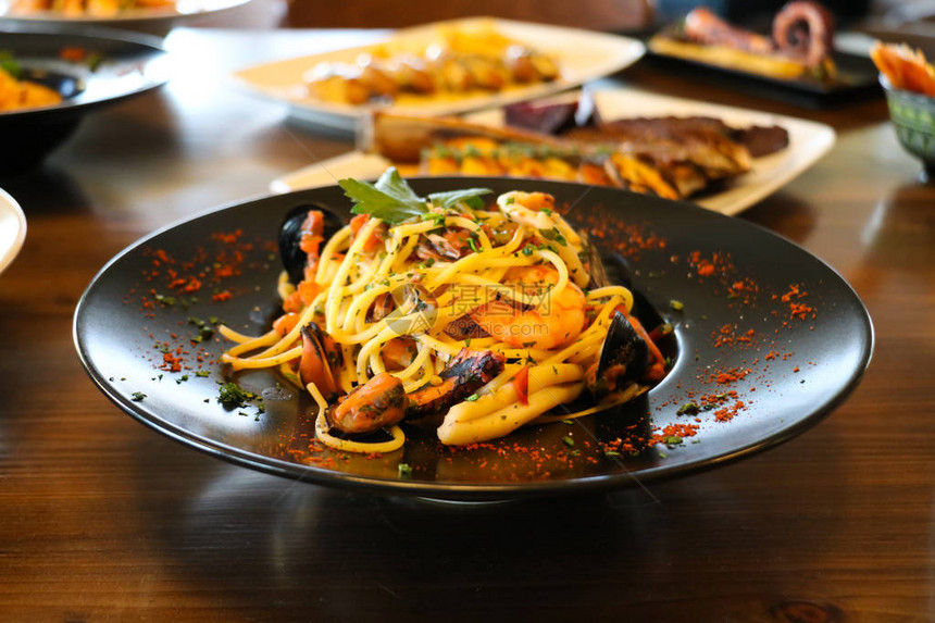 健康食品的概念黑盘上有虾贻贝和欧芹的意大利面用食物图片
