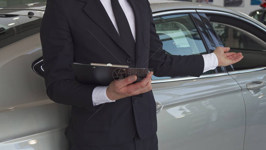 销售经理将手放在经销店的新车上的特写穿着黑色西装的男卖家手里拿着剪贴板的低镜头顾问提图片