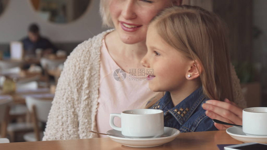 漂亮的金发女人在咖啡馆里给女儿看东西有吸引力的小女孩和她的母亲看着副本的地方可爱的白人妈在桌边拥抱她图片