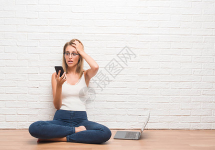 美丽的年轻女子坐在地板上用智能手机和笔记本电脑发短信图片