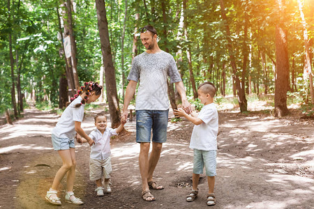 快乐的父亲带着孩子们在阳光明媚的夏日森林里牵着手爱图片