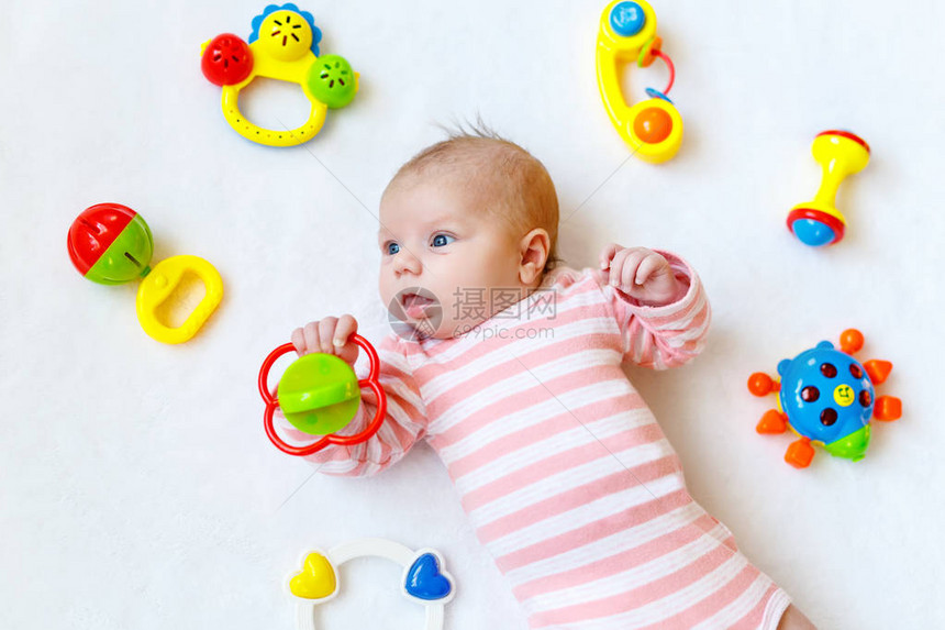 可爱的新生婴儿在白色背景上玩很多五颜六色的拨浪鼓玩具图片