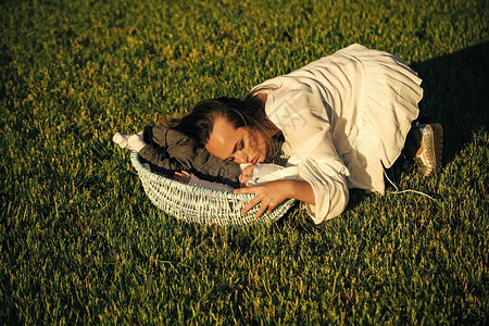 妈抱着小儿子在绿草地上的婴儿床里睡着了女人睡在户外篮子里的婴儿男孩的概念家庭爱保护信任做梦背景图片