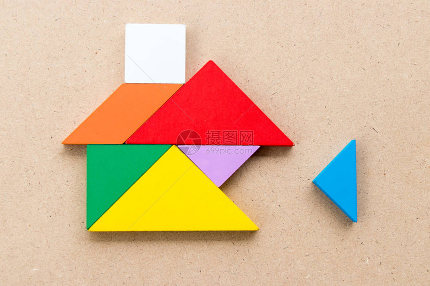 在木背景上等待三角拼图以完成家庭形状的彩色tangram拼图关于建造梦想屋幸福家庭或按揭图片