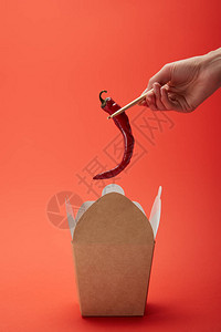 红色盒上方的筷子中握着辣椒图片