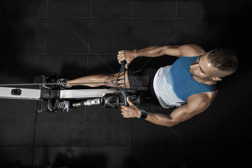 上面的体育运动员腿假肢在健身房打划船机工作他正在图片