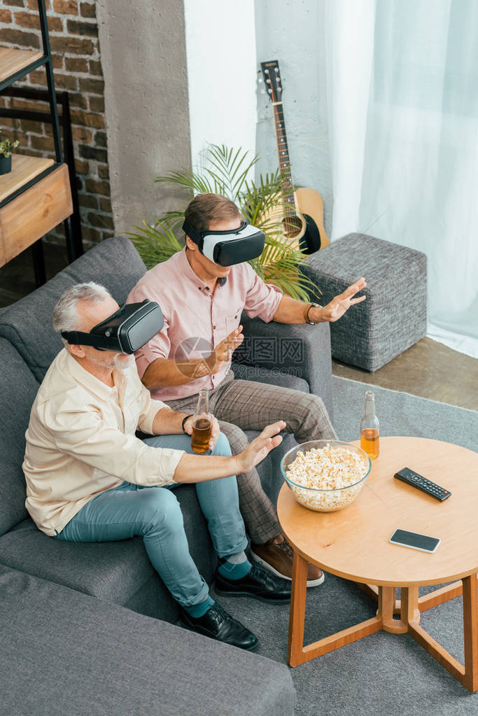 成年男子在坐沙发上喝啤酒和使用虚拟现实头戴耳机时图片
