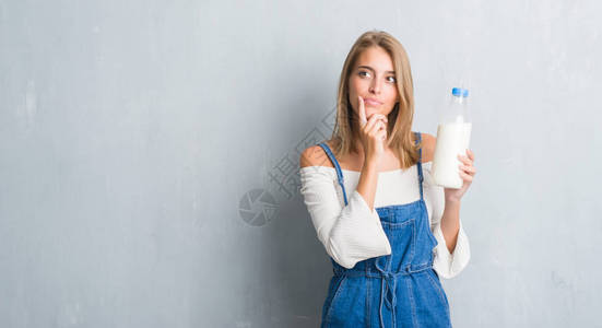 美丽的年轻美女在黑灰墙上拿着一瓶新鲜牛奶面对着严肃的面孔思考问题图片