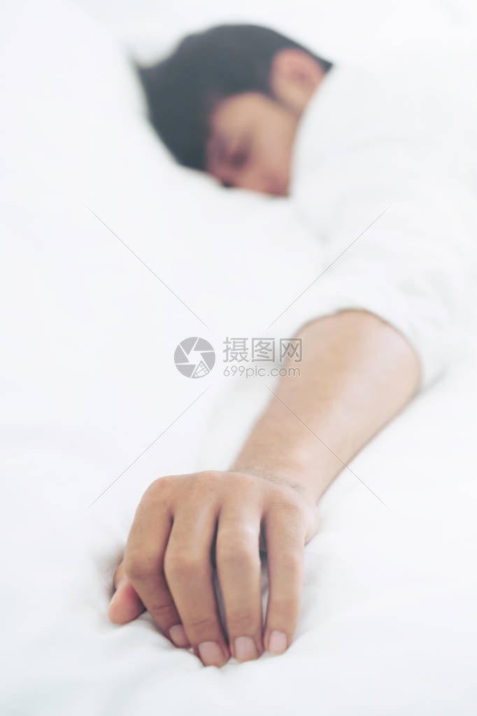 年轻人睡在卧室的白色亚麻床上图片
