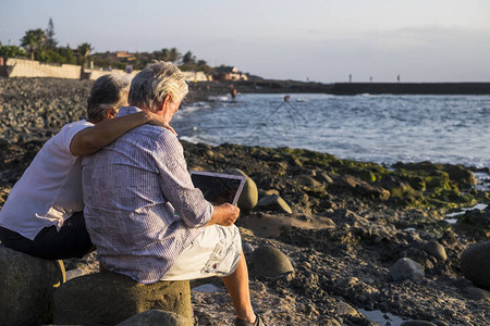 快乐的老年情侣与平板电脑在石子海滩上图片