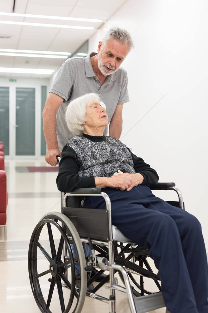 中年男子帮助和陪伴坐在轮椅上的95岁老年妇女退休公民概图片