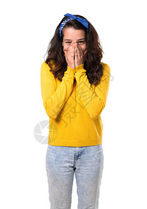头上戴黄色毛衣和蓝带的年轻女孩在用孤立的白色背景遮住嘴唇时图片