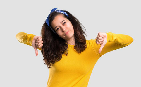 头上戴黄色毛衣和蓝带的年轻女孩用两只手举起拇指向下图片
