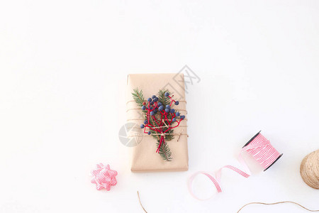 圣诞新年礼物用工艺纸和浆果装饰在丝带和蝴蝶结旁边的白色背景上图片