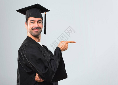 在毕业日的男士大学用手指对准方以灰色背景平面姿势展示一图片