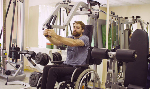 坐在轮椅上的年轻残疾人在康复诊所进行手部力量锻炼帮助他的医图片
