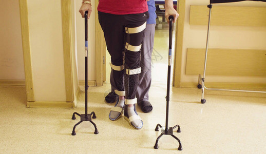 在康复诊所用两根拐杖支撑行走矫形器的残疾人的腿图片