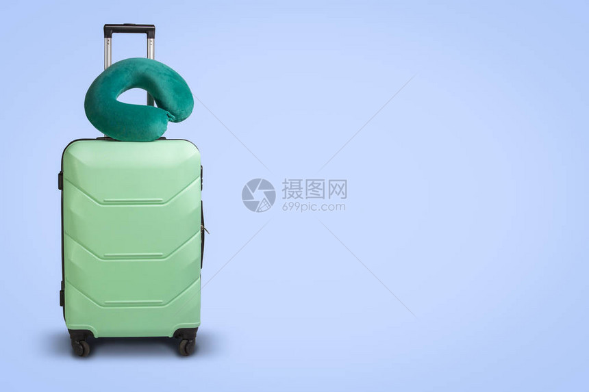蓝色背景上的塑料手提箱和旅行枕头旅行商务旅行探图片