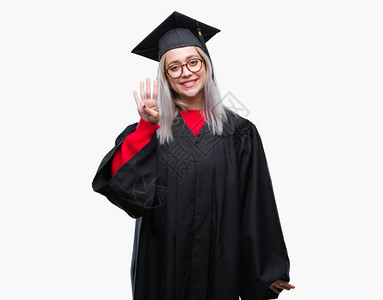 身穿毕业制服的金发年轻女郎在孤立的背景展出和指着四号手指时微笑着自信图片