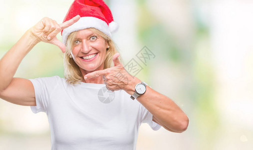 穿着圣诞帽的中年金发女郎在孤立的中微笑地用手和指搭架图片