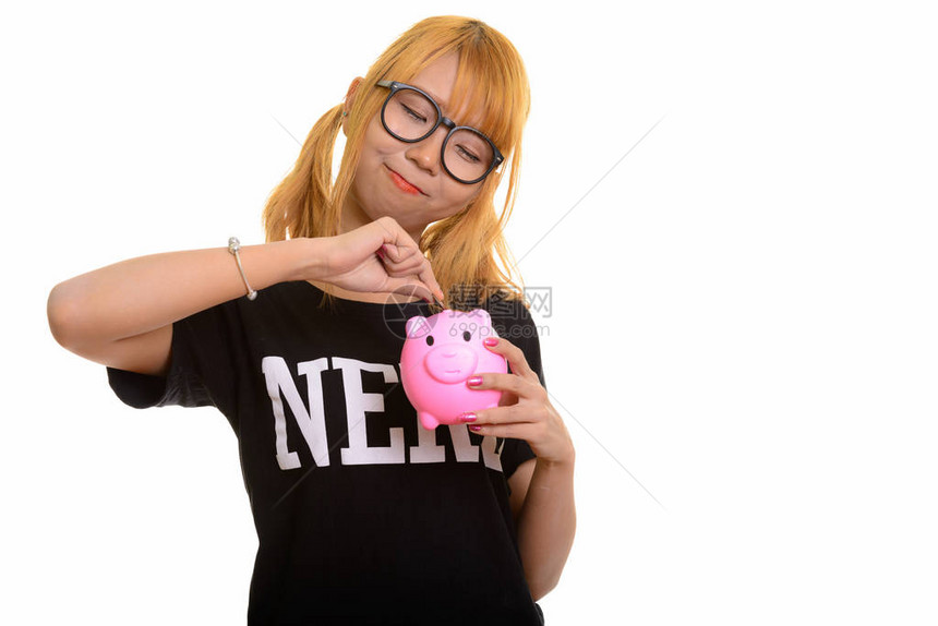 年轻可爱的亚洲书呆女把硬币放进小猪银行在白种图片