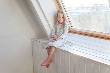 穿着白裙子的可爱甜蜜笑脸女孩坐在窗边图片