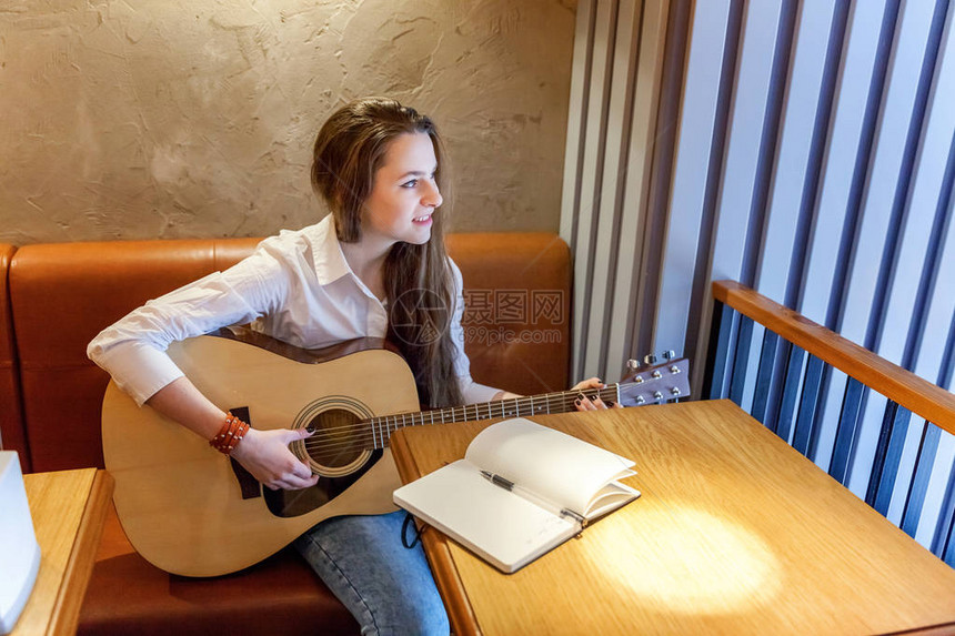 坐在咖啡馆弹吉他和写歌的年轻笑嬉皮士女青年图片