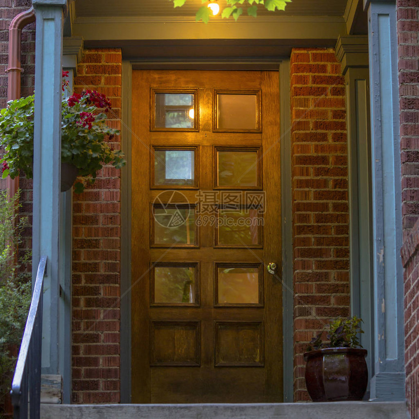 带玻璃镶板棕色木前门的砖房对有红砖墙和观赏盆栽植物的房子的入口带金属栏杆的楼梯通向带玻璃图片