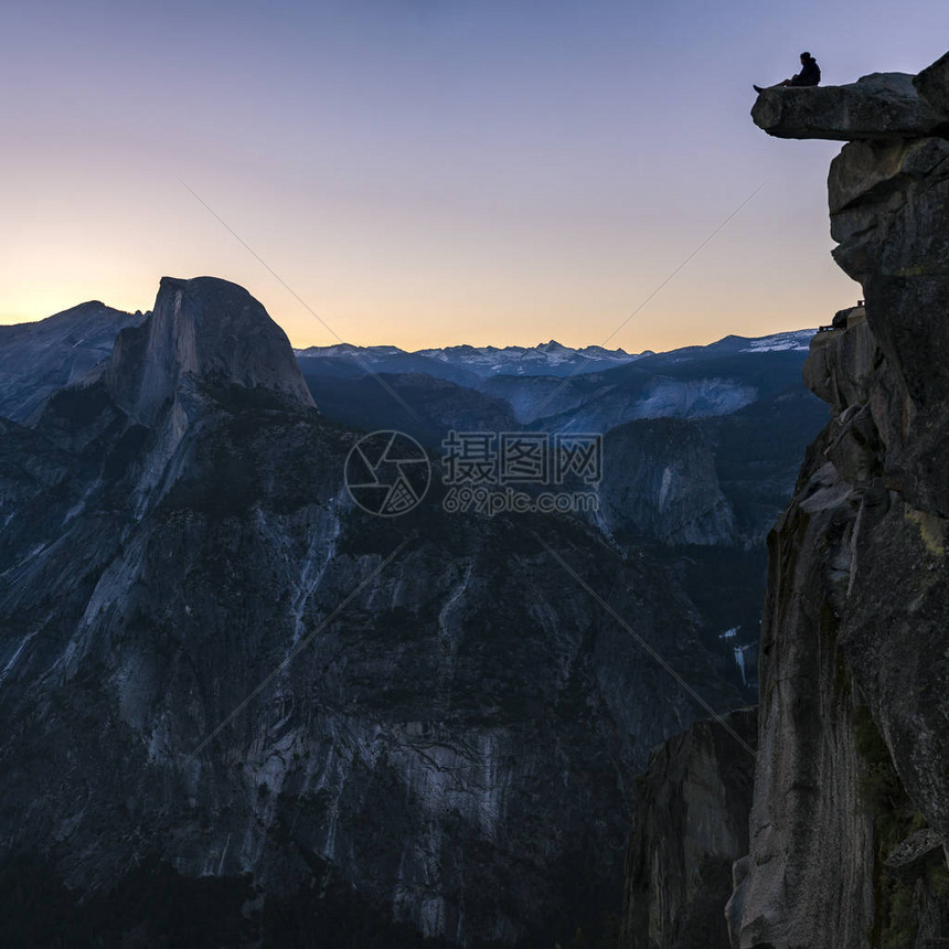 坐在优胜美地悬崖边缘的人一个人坐在一个看起来非常高且危险的悬崖边缘他对加利福尼亚州优胜美地雄伟的岩山图片