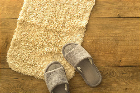 木制地板上贴着灰色家庭拖鞋的小型田地软蜜蜂地毯背景图片