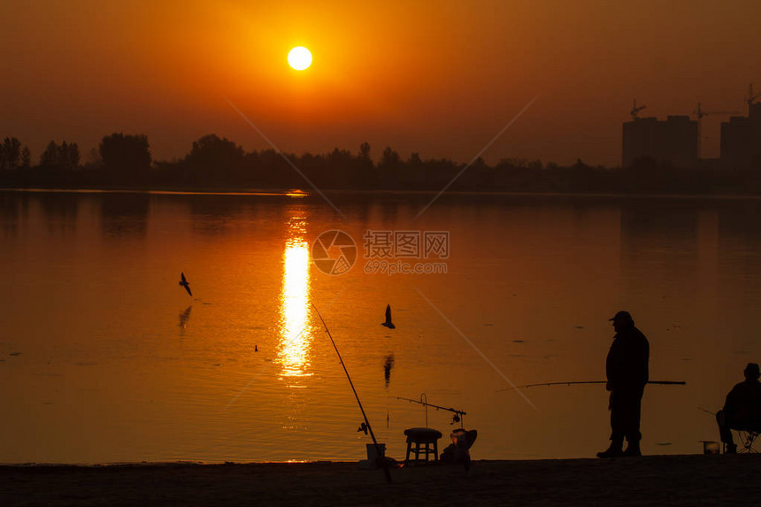 渔夫站在湖中在雾日出时抓鱼的剪影图片