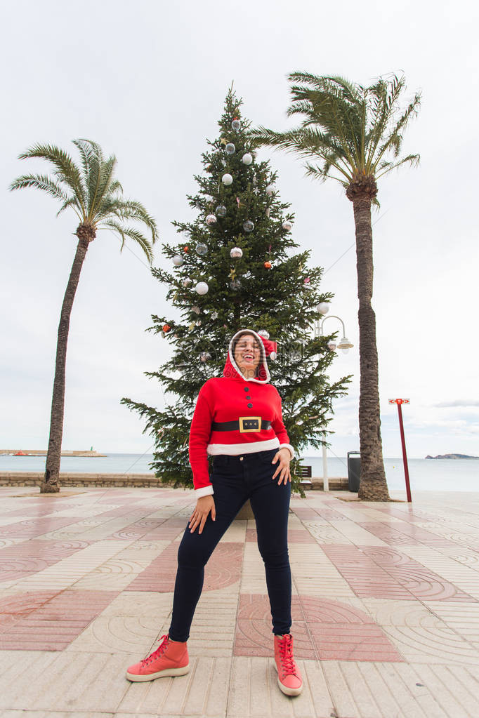 圣诞节假期和幽默的概念年轻快乐的女人在夏天在棕榈树和圣诞树附近穿着圣诞图片