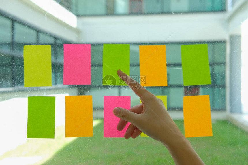 手指着工作场所玻璃墙上的胶粘剂便条用于创意和商业头脑风暴的便条图片