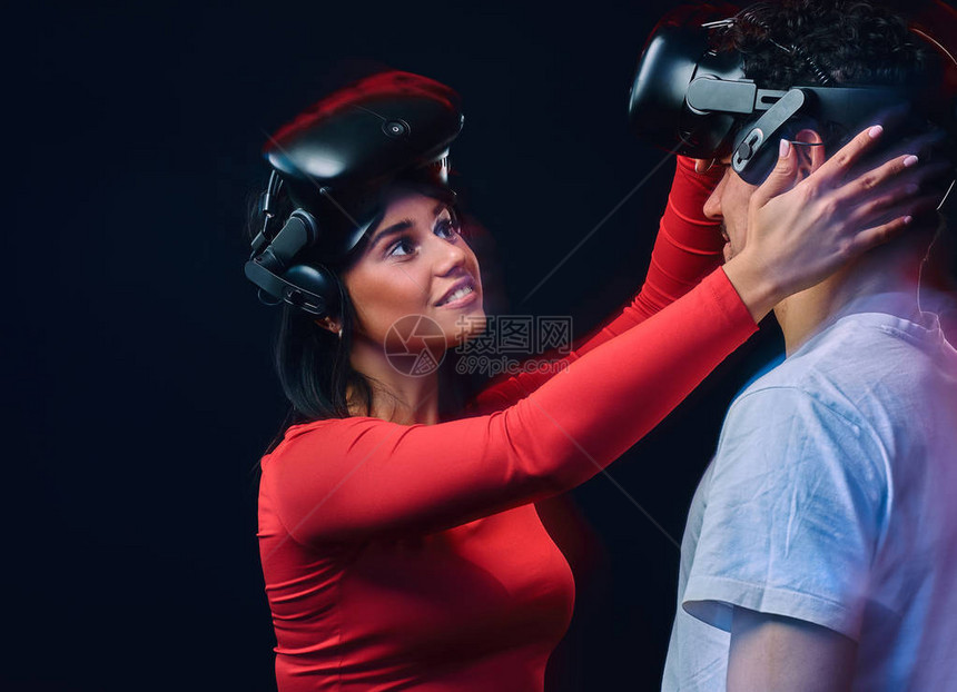 年轻快乐的女孩调整了虚拟现实眼镜在她的男朋友上两个有VR头盔的游戏家图片