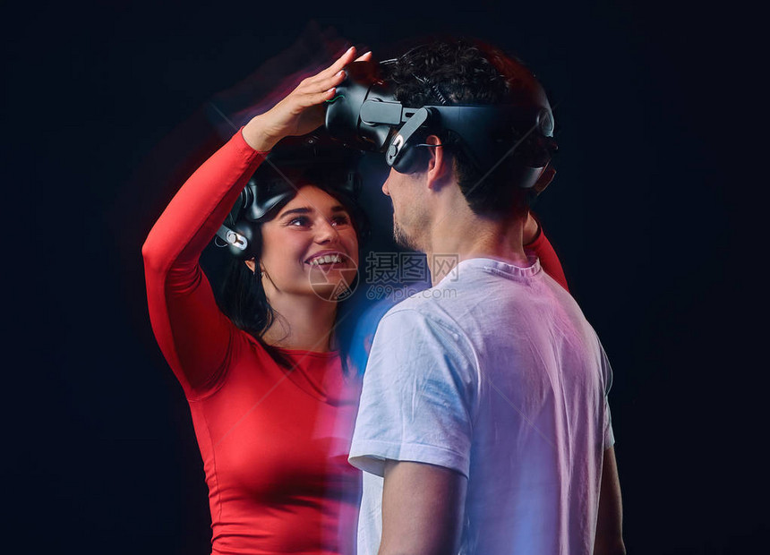 年轻快乐的女孩调整了虚拟现实眼镜在她的男朋友上两个有VR头盔的游戏家图片