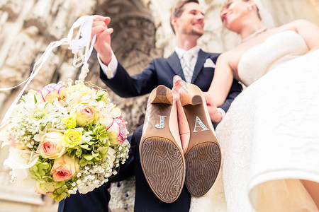 新郎捧着花束球和新娘展示婚礼鞋底的特写镜头背景图片