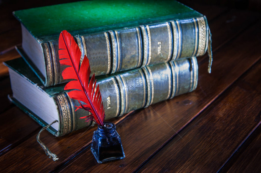 木桌上放着旧书的红色鹅毛笔和深色墨水瓶图片