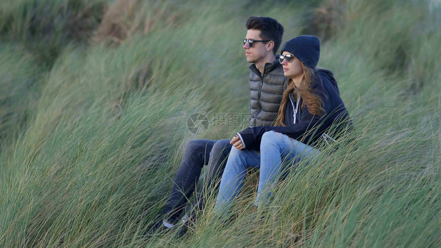 年轻夫妇坐在青草中享受海洋的呼声图片