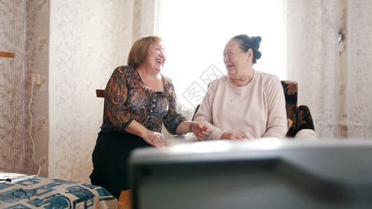 两个老年妇女在看电视互相看着对方笑图片