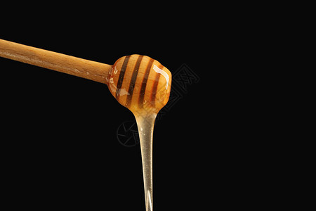 深色背景下从木勺里倒出的蜂蜜图片
