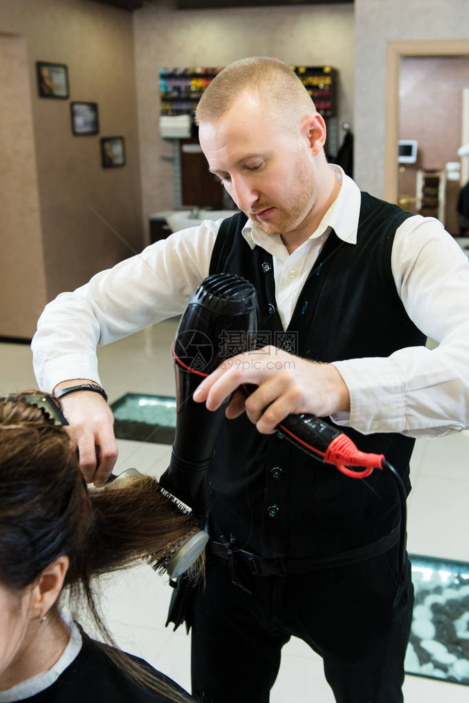 美发师用吹风机和圆刷吹干长的黑发一位整洁的发型师在他的专业工作室图片