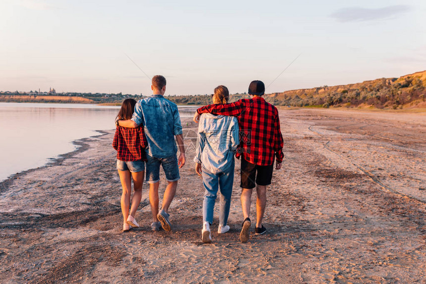 日落时在海滩上一起散步的一群潮湿的年轻朋友图片