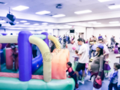 运动模糊多样的多民族儿童享受充气弹跳屋跃游戏美国德克萨斯州室内学校万圣节派对的父母和孩子背景图片