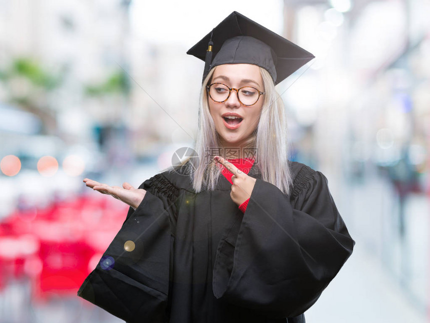 年轻的金发女子在孤立的背景下穿着研究生制服图片