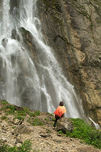 穿着橙色披肩的女人坐在瀑布附近她欣图片