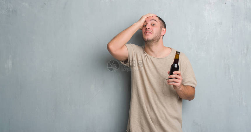 年轻的白人男子在灰色的垃圾墙上拿着瓶装啤酒图片
