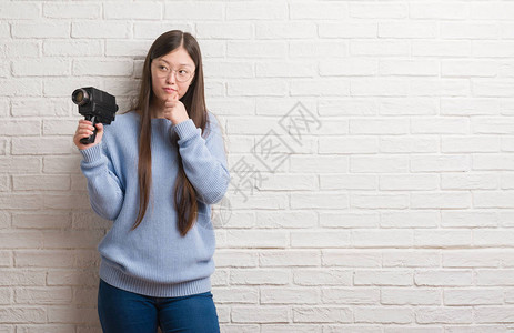年轻女拿着摄像机拍摄严肃的脸思考问题背景图片