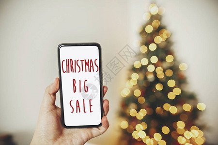 圣诞大销售文本假日折扣手持机在美丽的圣诞树背景上用灯光在节庆背景图片