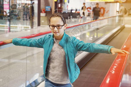 穿着眼镜和蓝色夹克的可爱小女孩站在机场移动扶梯上图片